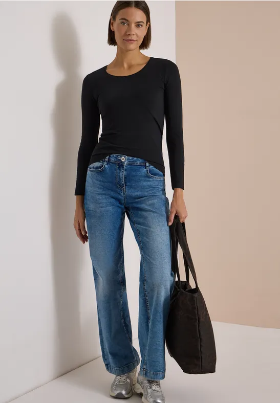 Femme en haut noir à manches longues et jean bleu droit, tenant un sac cabas noir.