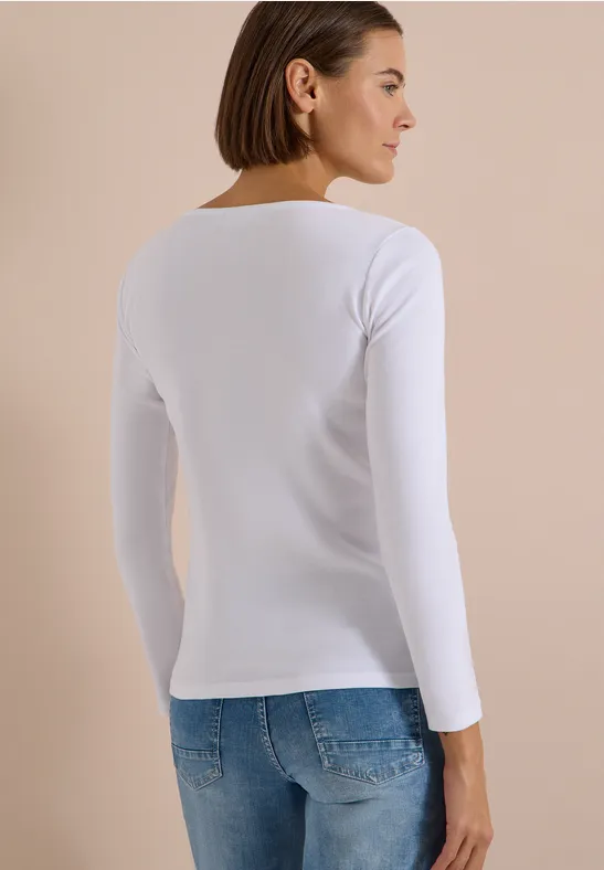 Femme de dos portant un t-shirt à manches longues blanc et un jean bleu sur fond discret.