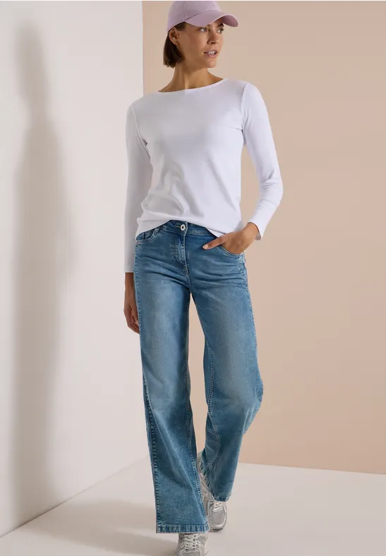 Mannequin porte un haut blanc à manches longues, jean bleu, baskets blanches et casquette violette devant un mur sobre.