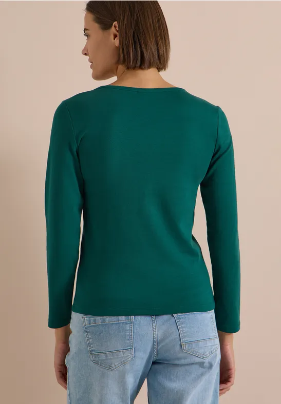 Rückenansicht einer Frau in grünem Langarmshirt und blauen Jeans.