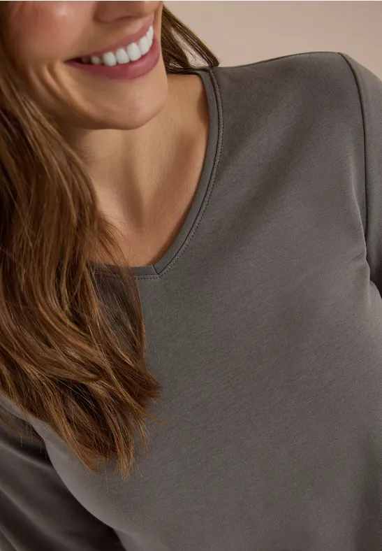 Nahaufnahme einer lächelnden Frau in einem grauen Langarmshirt.