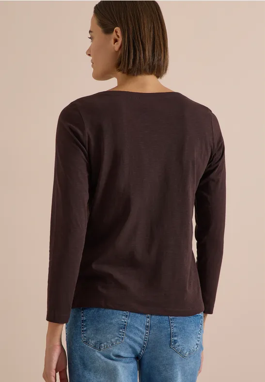 Frau von hinten in dunkelrotem Longsleeve und blauen Jeans vor neutralem Hintergrund
