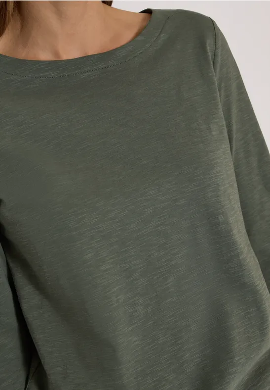 Frau trägt ein schlichtes olivgrünes Langarmshirt aus leicht strukturierter Baumwolle.