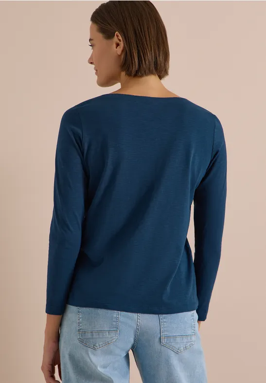 Frau in dunkelblauem Langarmshirt und hellblauen Jeans, seitlich von hinten gezeigt.