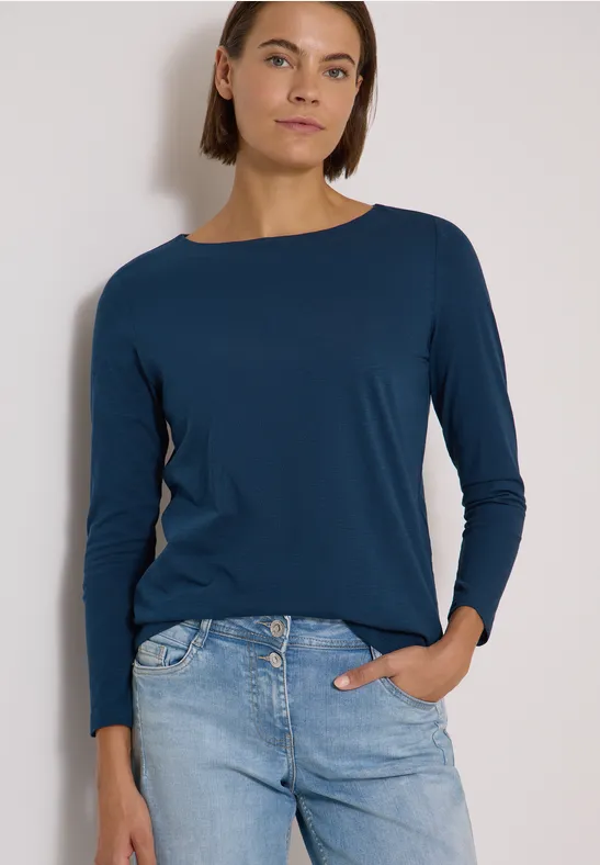 Frau trägt dunkelblaues Langarmshirt und Jeans, eine Hand in Tasche