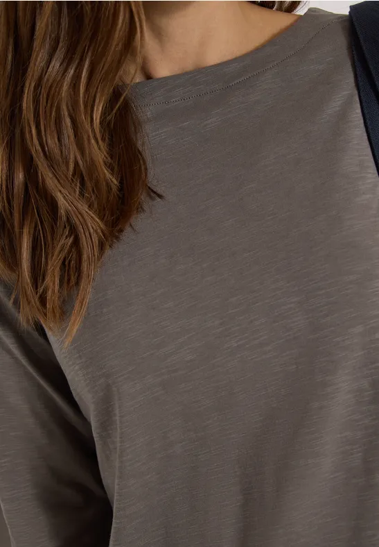 Frau in schlichtem grauen Langarmshirt mit weitem Rundhalsausschnitt.
