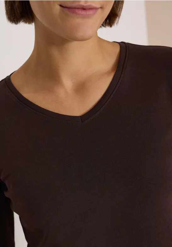Eine Frau trägt ein dunkelbraunes, langärmliges Shirt mit V-Ausschnitt.