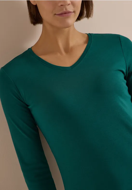 Frau in grünem V-Ausschnitt-Langarmshirt, Oberkörperaufnahme.