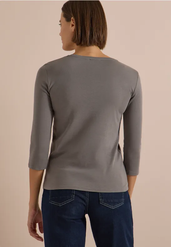 Frau von hinten in grauem Langarmshirt mit 3/4-Ärmeln und blauen Jeans.