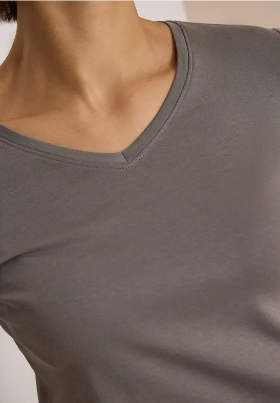 Nahaufnahme des Oberkörpers in einem schlichten grauen V-Ausschnitt-Shirt vor neutralem Hintergrund.