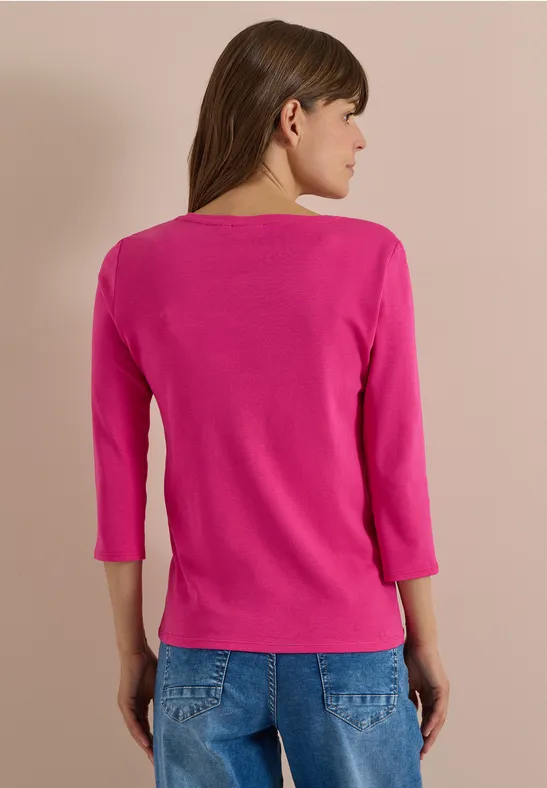 Rückansicht einer Frau in pinkem Dreiviertel-Arm-Shirt und blauen Jeans.