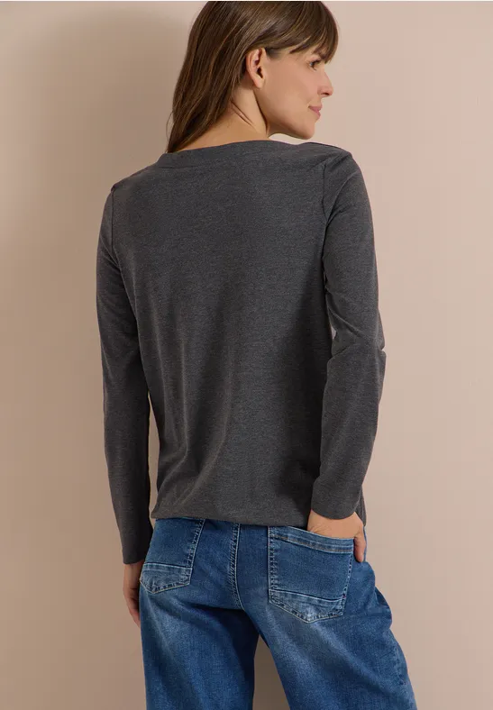 Frau von hinten in grauem Langarmshirt und lockeren blauen Jeans, Hände in den Taschen, braune Haare.