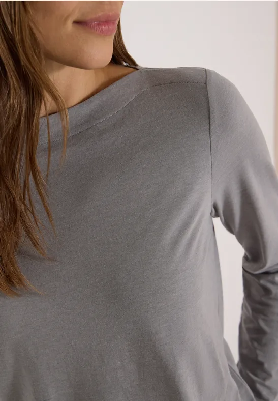 Vorderansicht einer Frau in grauem Langarmshirt, Oberkörper und Teil des Gesichts sichtbar.
