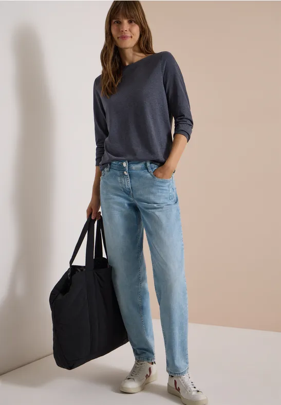 Vrouw met donkerblauwe trui, lichte jeans en witte sneakers, met een grote zwarte tas.