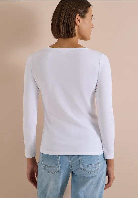 Frau von hinten in weißem Langarmshirt und Jeans vor beigem Hintergrund.