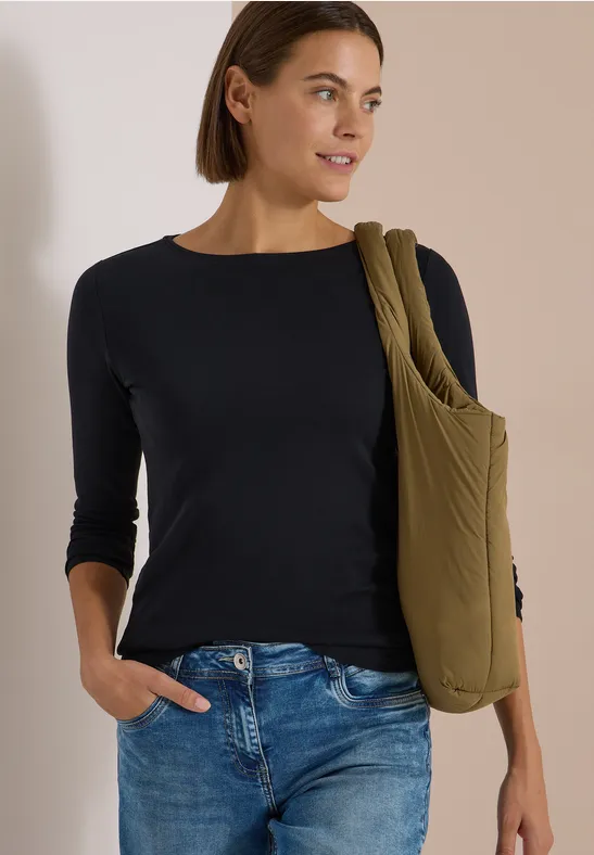 Frau trägt schwarzen Dreiviertelarm-Pullover, Jeans und eine olivgrüne Umhängetasche.
