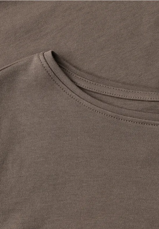 Nahaufnahme gestapelter, beigebrauner Baumwoll-T-Shirts mit sichtbaren Nähten am Rundhalsausschnitt.