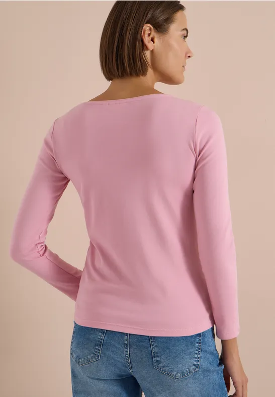 Frau von hinten in rosa Langarmshirt und blauen Jeans vor neutralem Hintergrund.