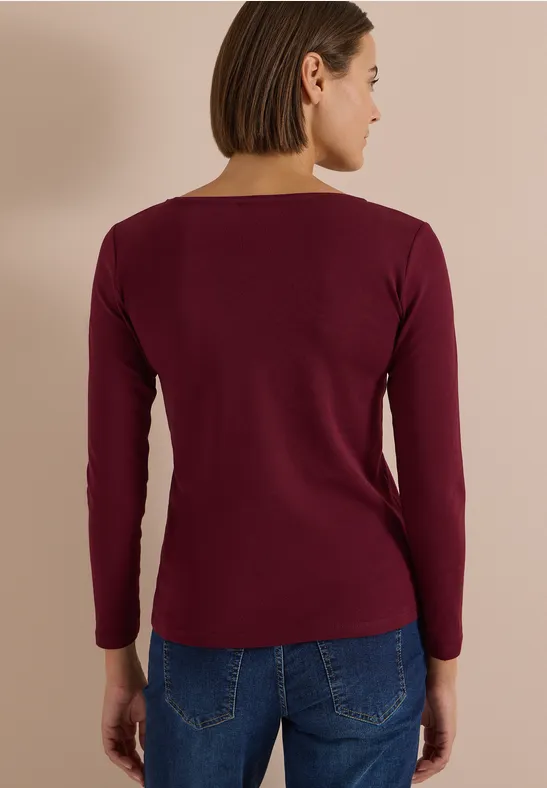 Rückansicht einer Frau in burgunderrotem Langarmshirt und Jeans
