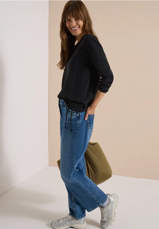 Femme en pull noir, jeans bleus amples, baskets blanches et sac vert.