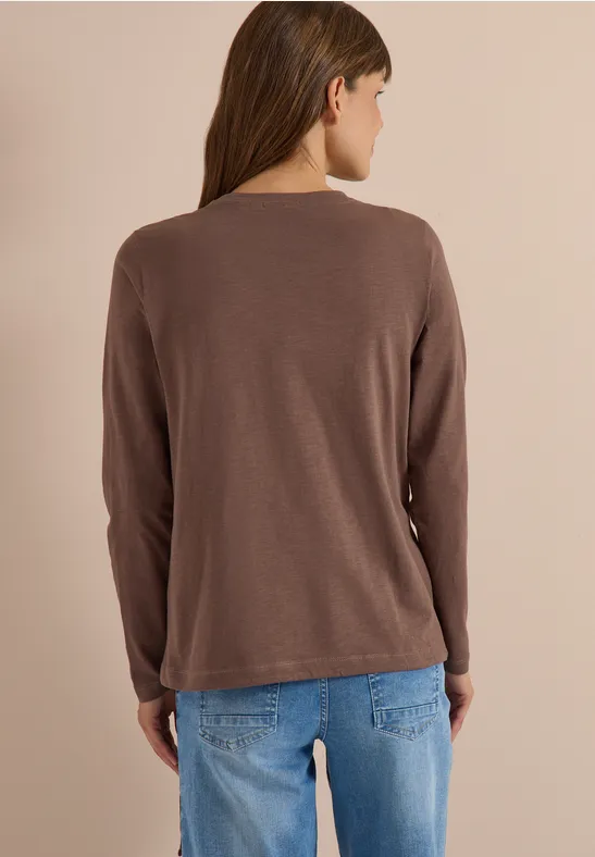 Dos d’une femme portant un t-shirt à manches longues marron et un jean bleu sur fond clair.