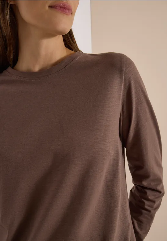 Gros plan sur le torse d’une personne portant un t-shirt à manches longues brun sur fond neutre.