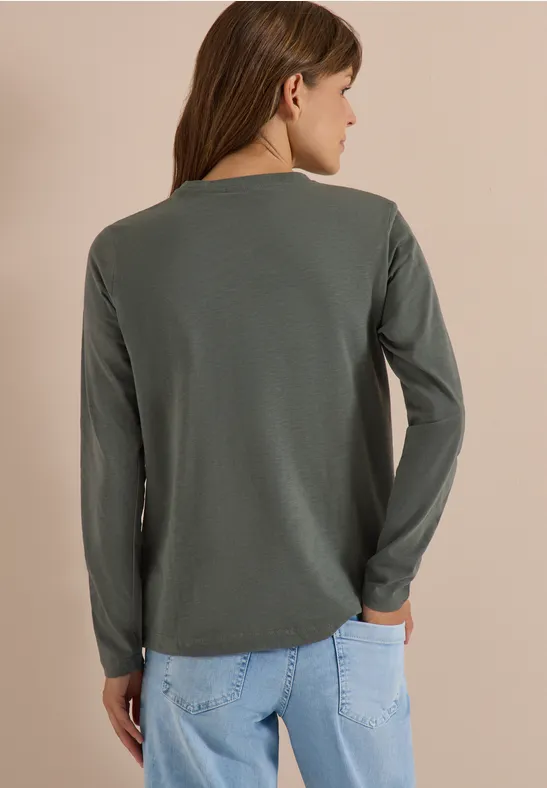 Vue de dos d'une femme portant un haut vert olive à manches longues et un jean bleu clair sur fond neutre.