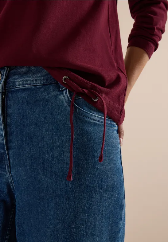 Person porte un haut rouge sombre et un jean ample avec un cordon à la taille.