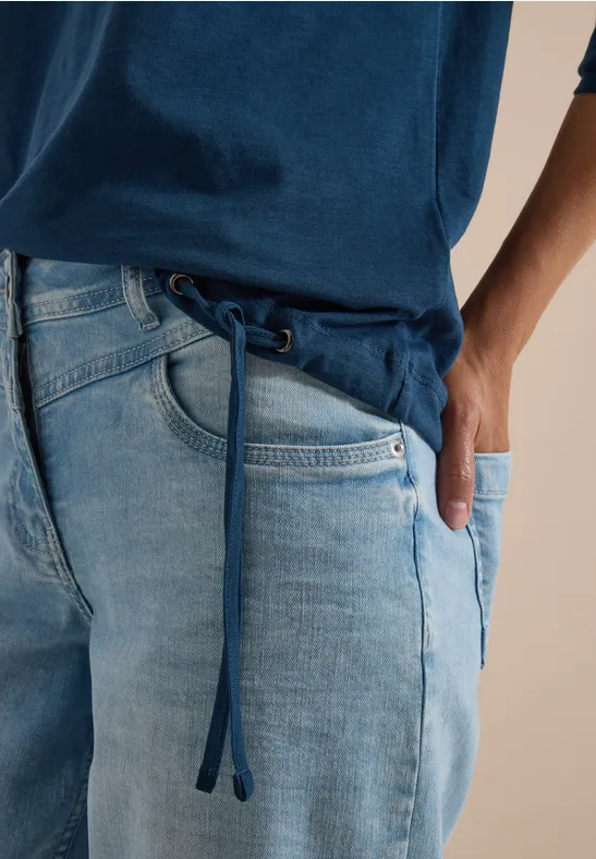 Person trägt eine hellblaue Jeans mit Tunnelzug und blaues T-Shirt.