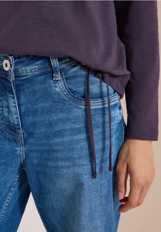 Eine Person in blauen Jeans und dunkelblauem Langarmshirt mit Kordeln.