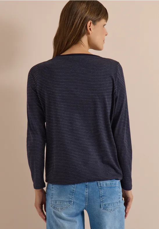Femme vue de dos portant un haut à manches longues bleu foncé à fines rayures et un jean bleu clair.