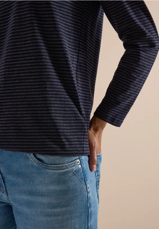 Vue partielle d'une personne en t-shirt à rayures et jean, main dans la poche.