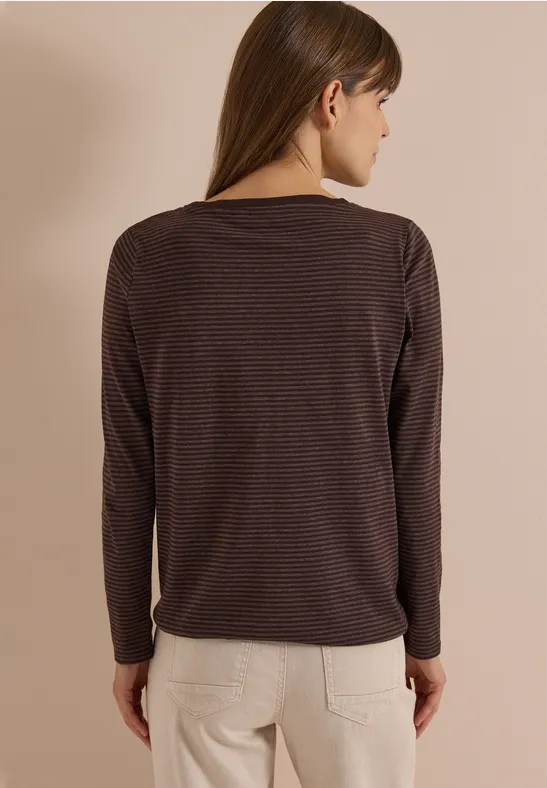 Frau von hinten in braun gestreiftem Langarmshirt und beigen Hosen vor beigem Hintergrund.