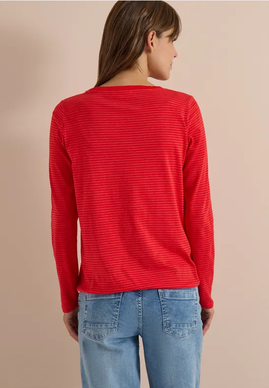 Une femme de dos portant un pull rouge et un jean bleu