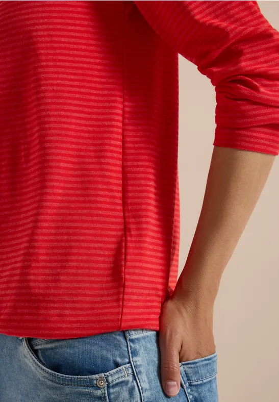 T-shirt à manches longues rouge rayé, main dans la poche d'un jean.