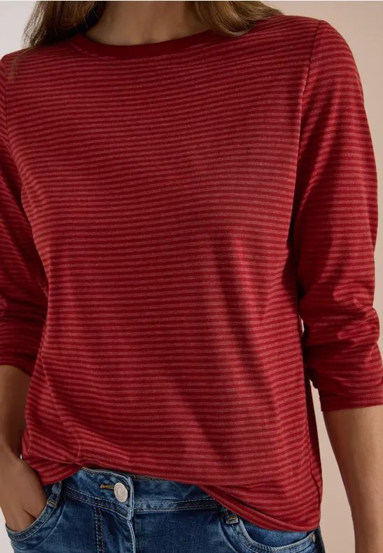 Rotes, langärmliges, gestreiftes Oberteil an einer Person, kombiniert mit Jeans.