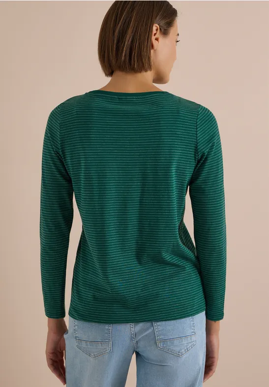 Rückenansicht einer Frau in grün geringeltem Langarmshirt und hellblauer Jeans vor beigem Hintergrund.