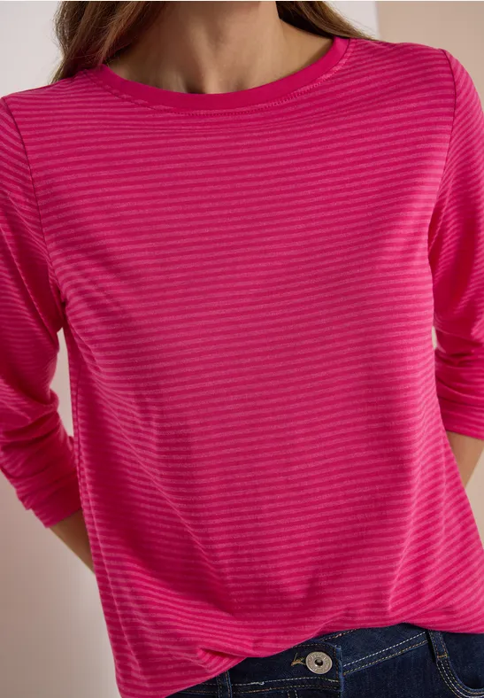 Eine Person trägt ein pink gestreiftes Langarmshirt und blaue Jeans.