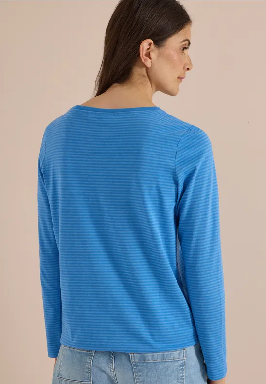Frau von hinten in blau-weiß gestreiftem Langarmshirt und Jeans vor beigem Hintergrund.