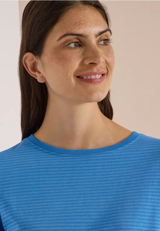 Junge Frau mit dunklen Haaren und blau gestreiftem Shirt lächelt zur Seite.