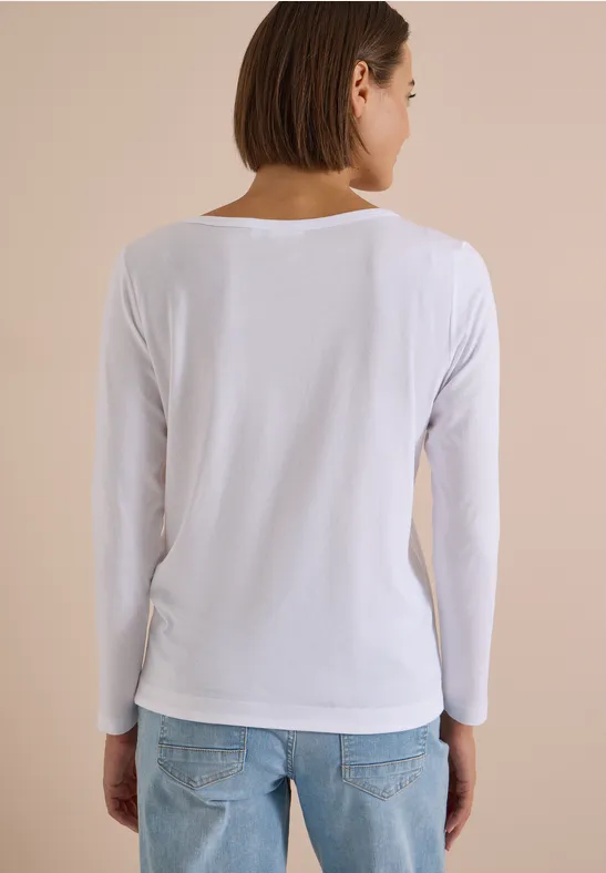 Frau von hinten in weißem Langarmshirt und Jeans vor hellbeigem Hintergrund.