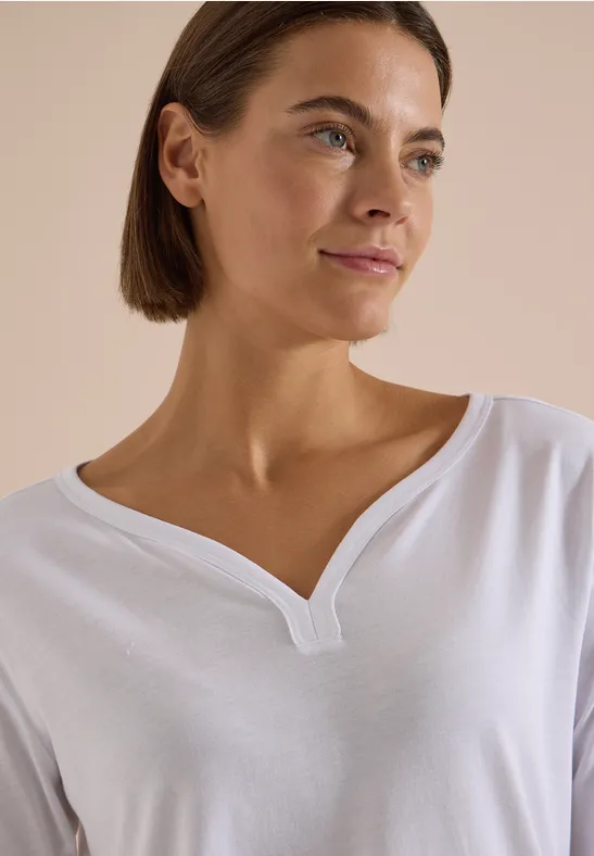 Portrait einer Frau mit kurzen braunen Haaren in einem weißen Shirt mit V-Ausschnitt.