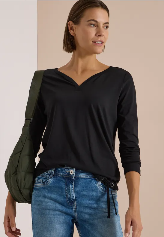 Frau trägt schwarzen V-Ausschnitt-Top mit langen Ärmeln, Jeans und grüner Schultertasche.