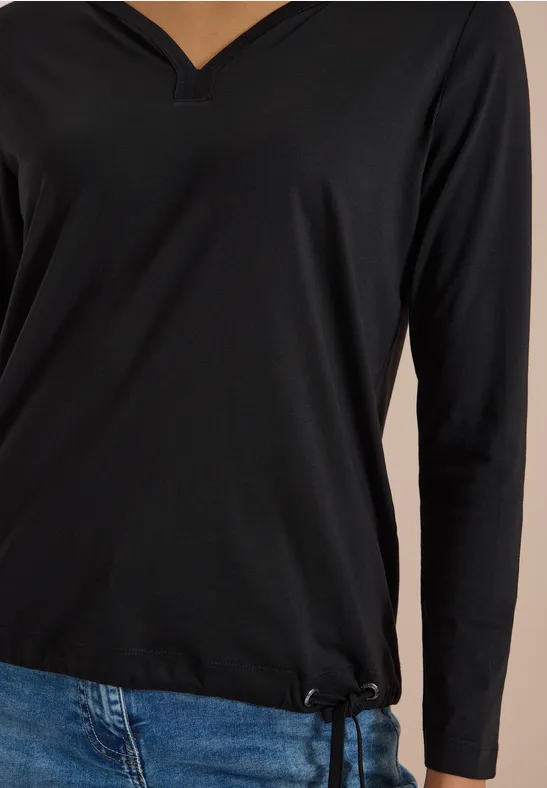 Schwarzes V-Ausschnitt-Langarmshirt kombiniert mit blauen Jeans, Ansicht der Oberkörperpartie.