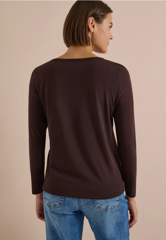 Rückansicht einer Frau mit kurzen Haaren in langärmeligem braunem Oberteil und hellblauen Jeans.