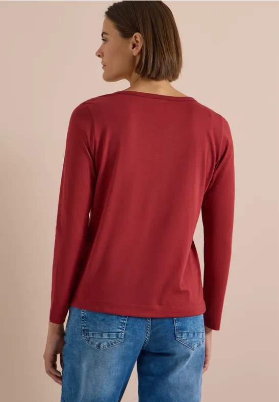 Rückenansicht einer Person mit rotem Langarmshirt und blauer Jeans vor beigefarbenem Hintergrund.