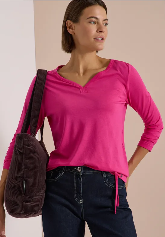 Frau trägt pinkes Langarmshirt, dunkle Jeans und eine Schultertasche.