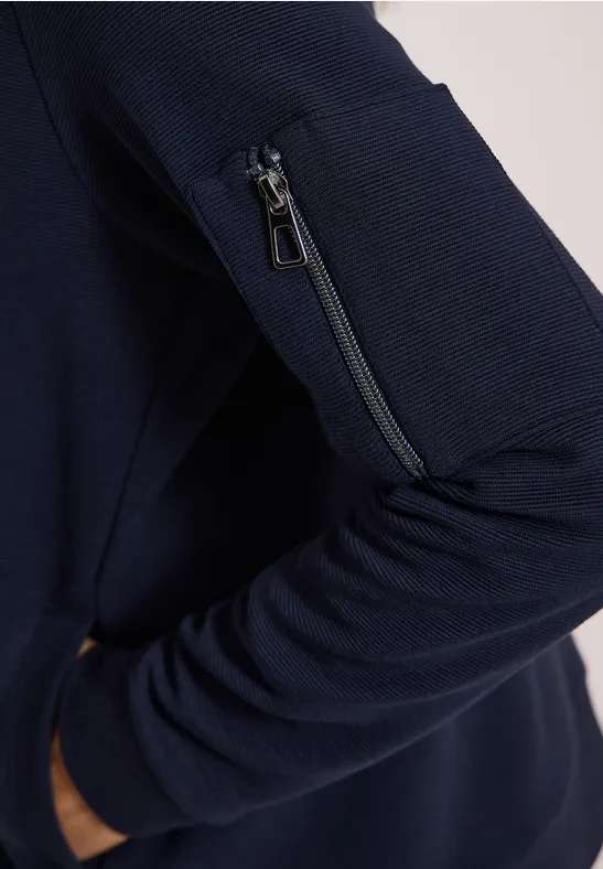 Dunkelblauer Pullover mit Reißverschlusstasche am Ärmel und seitlicher Eingriffstasche.