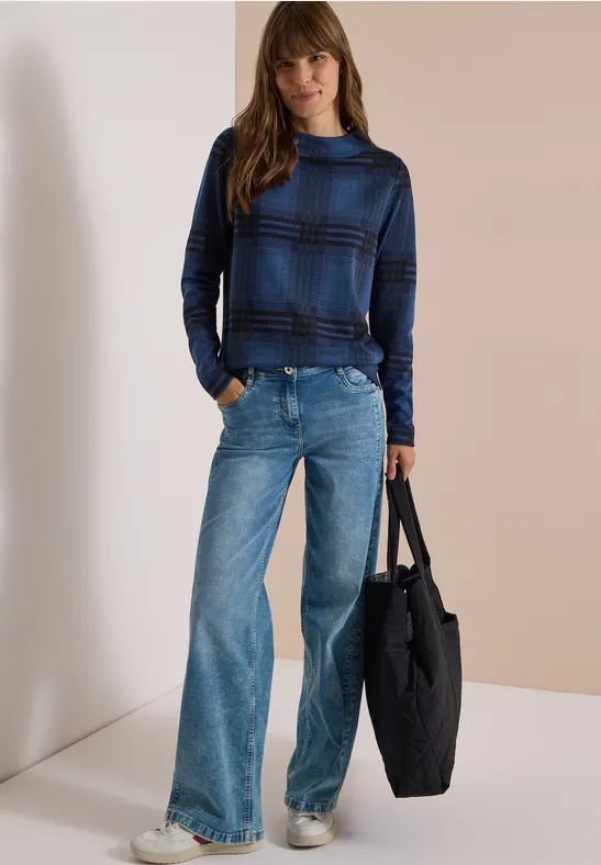 Eine Frau in blauem Rollkragenpullover und weiten Jeans hält eine große schwarze Tasche