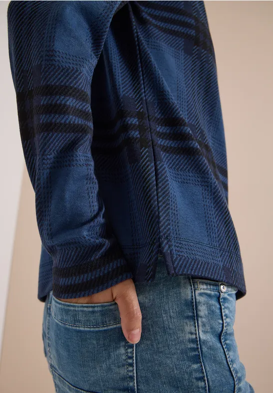 Seitliche Ansicht eines Oberkörpers mit blau kariertem Shirt und Jeans, Hand in Tasche.